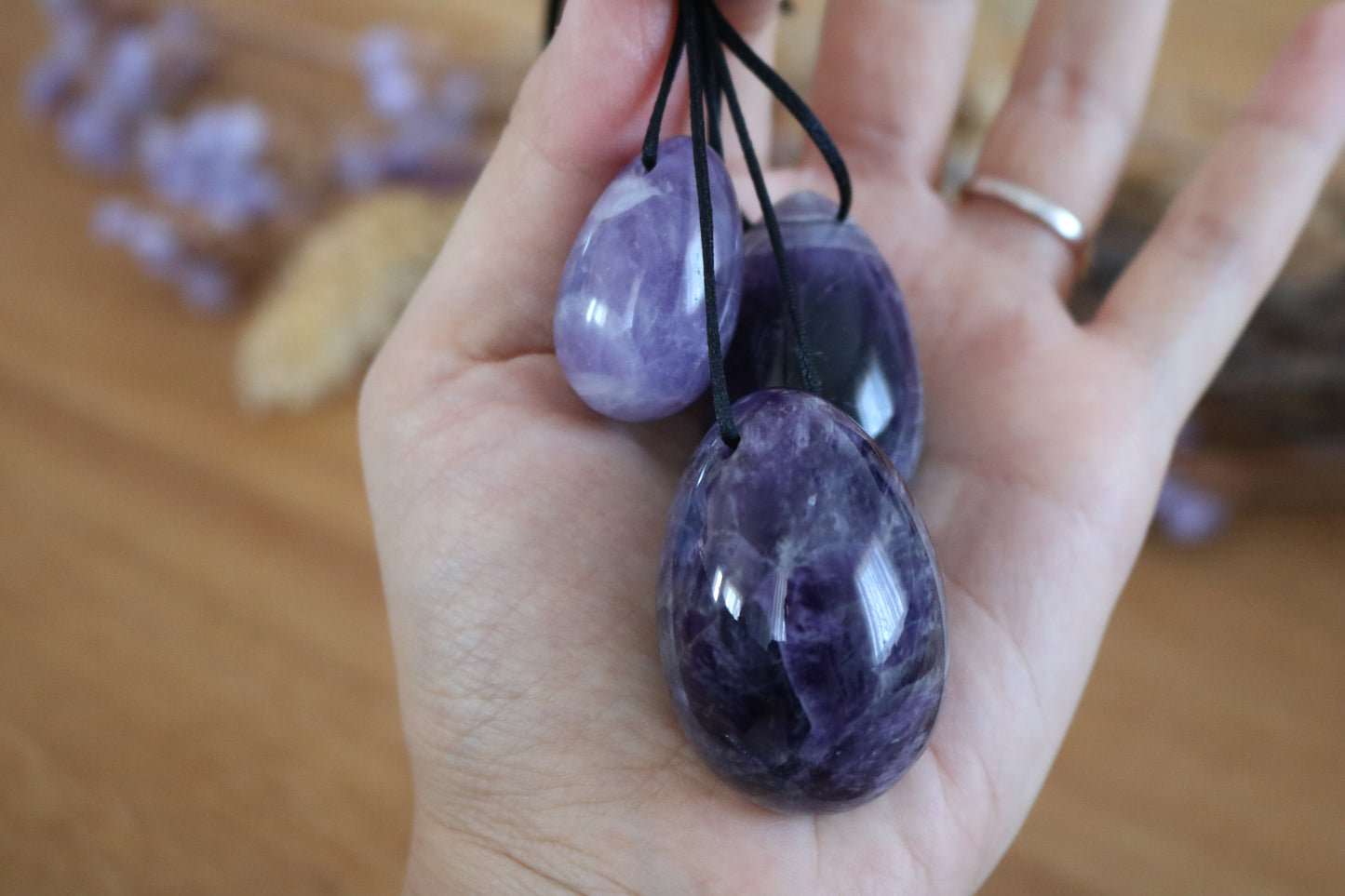 Hand holding 3 amethyst Yoni Eggs with black cords