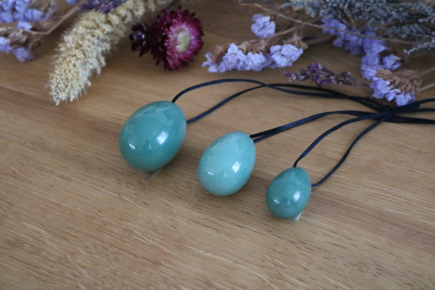 Three Green aventurine Yoni Eggs on a wooden surface with dried flowers in the background