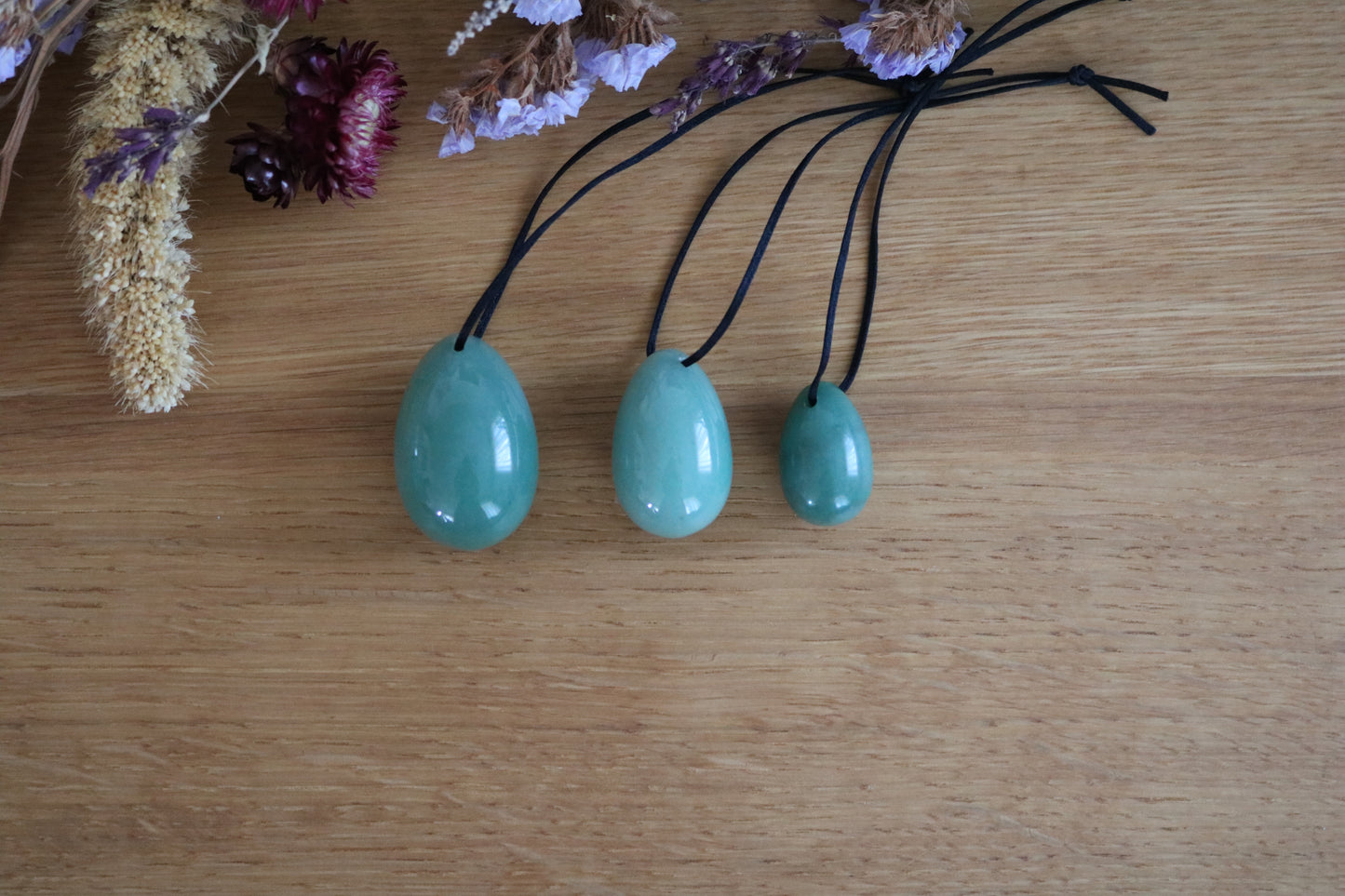 Three green aventurine pendants on black cords with dried flowers on a wooden surface