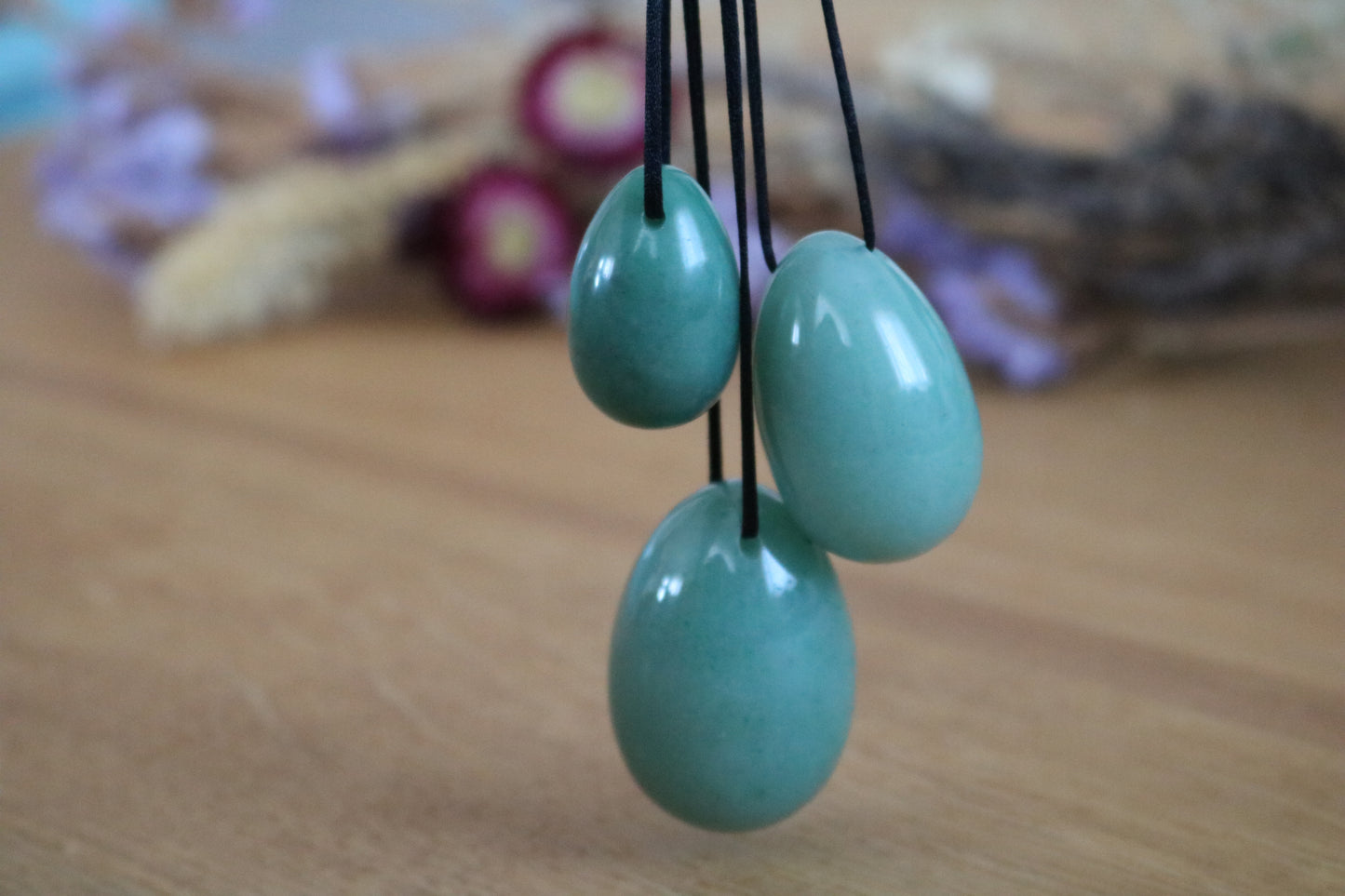 Three Green aventurine yoni eggs beads hanging on black cords against a blurred background
