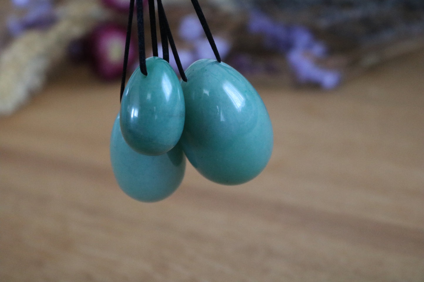 Three Green aventurine Yoni eggs on black strings against a blurred background