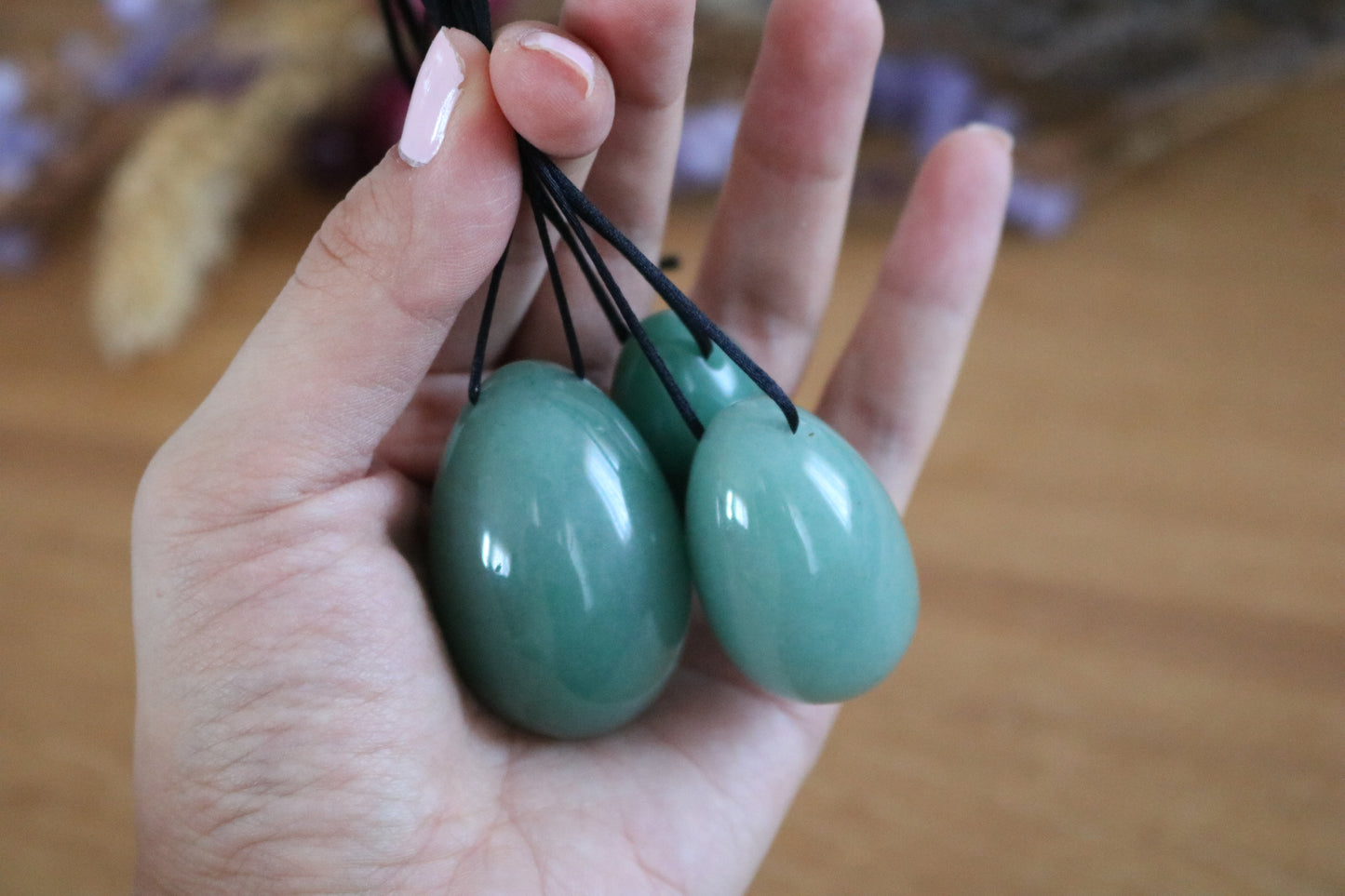 Hand holding tree green aventurine yoni eggs against a blurred background