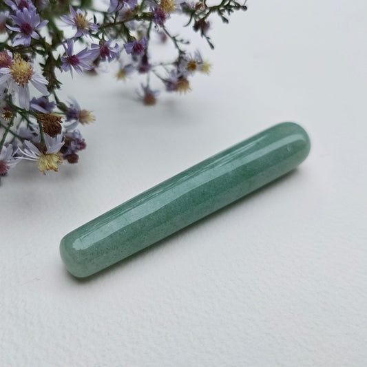 A polish mini green aventurine yoni wand for spiritual stimulation on a white textured surface with wildflowers