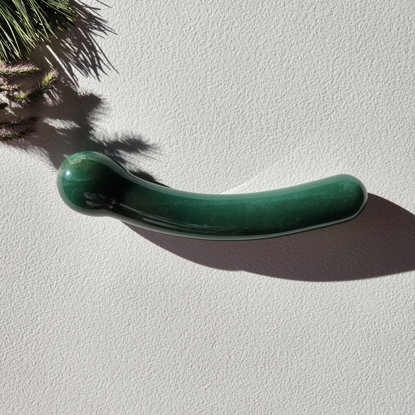 Crystal Wand Yoni Curved Green on a white surface in a shadow