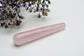 A polished pink rose quartz crystal wand lies on a white surface next to wildflowers.