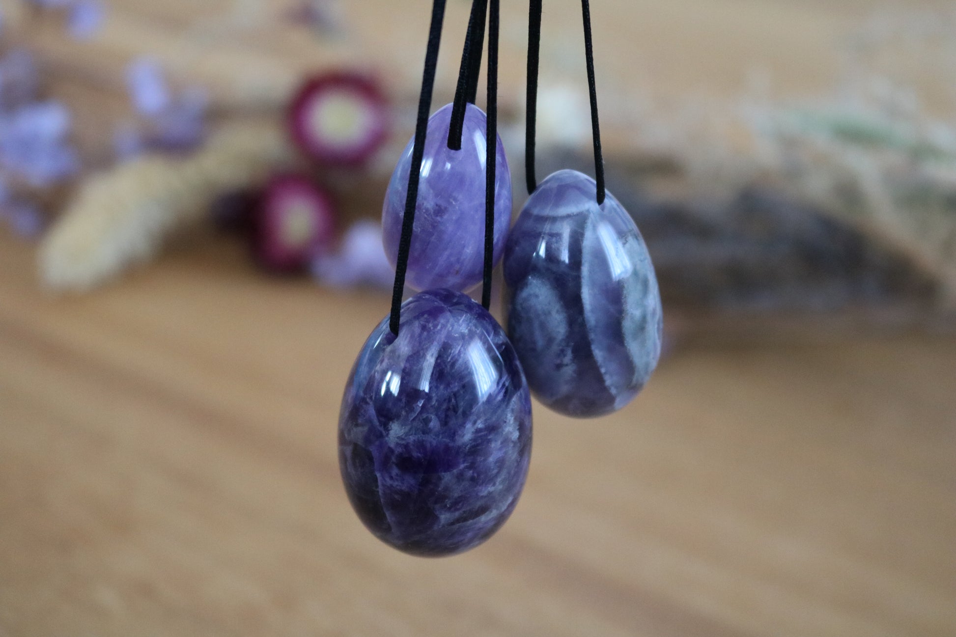 Amethyst Yoni Eggs set pendants on black cords against a blurred natural background