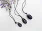 A set of three polished Amethyst yoni eggs in varying shades of purple lying on a white textured surface with wildflowers.