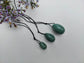 A set of three polished Green Aventurine yoni eggs, with black cords, lying on a white textured surface with wildflowers.