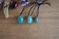 Three green aventurine pendants on black cords with dried flowers on a wooden surface