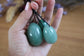 Hand holding tree green aventurine yoni eggs against a blurred background