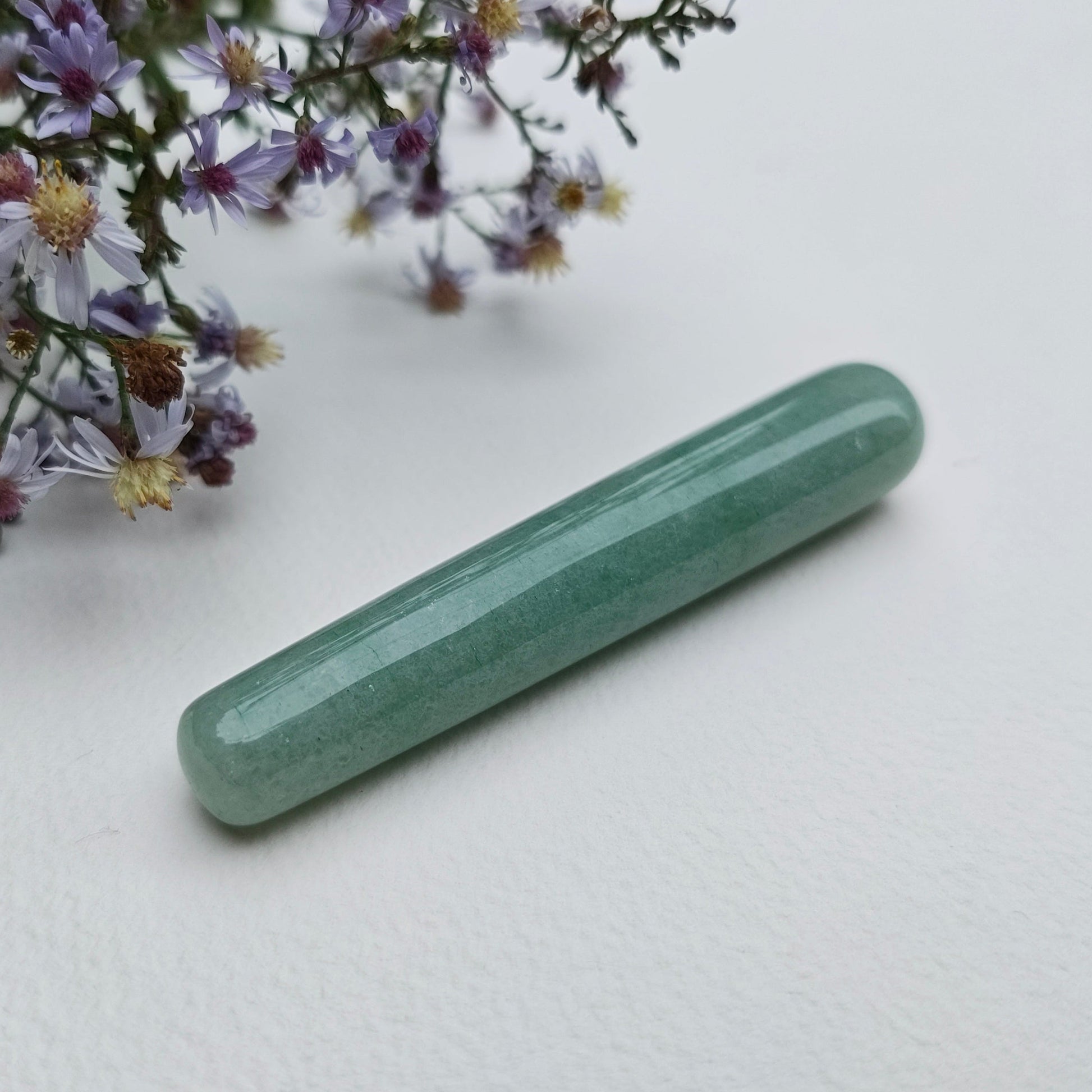 A polish mini green aventurine yoni wand for spiritual stimulation on a white textured surface with wildflowers