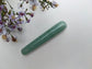 Mini green aventurine yoni wand for spiritual stimulation on a white textured surface with wildflowers