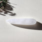 A close-up, of a large, straight, smooth Clear Quartz Yoni Wand. The lighting highlights the polished, reflective surface and the cloudy white interior with internal fractures. It is set against a light, textured background, and a sprig of dried grass. Perfect for anal stimulation