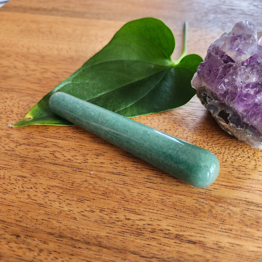 Mini green aventurine yoni wand for anal stimulation on a wood surface with leaves and crystal