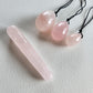 A set of three polished rose quartz yoni eggs with black strings and a smooth rose quartz mini wand, lying on a white textured surface.