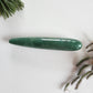 Polished green aventurine crystal yoni wand with a smooth, tapered shape to reach the G-Spot, shown on a white background with pine needles and dried grass.