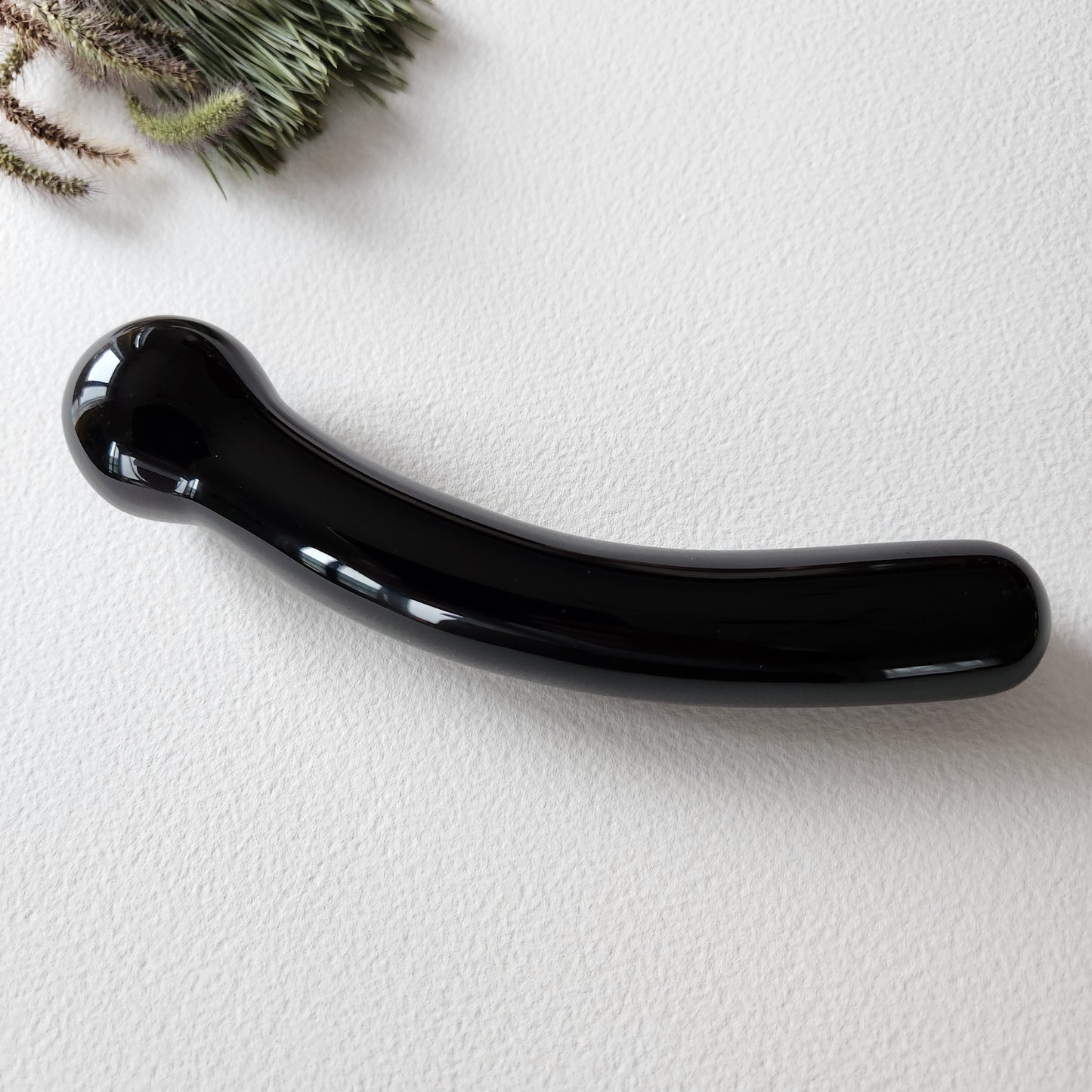 Close-up of a smooth, black curved obsidian crystal massage wand with round tip