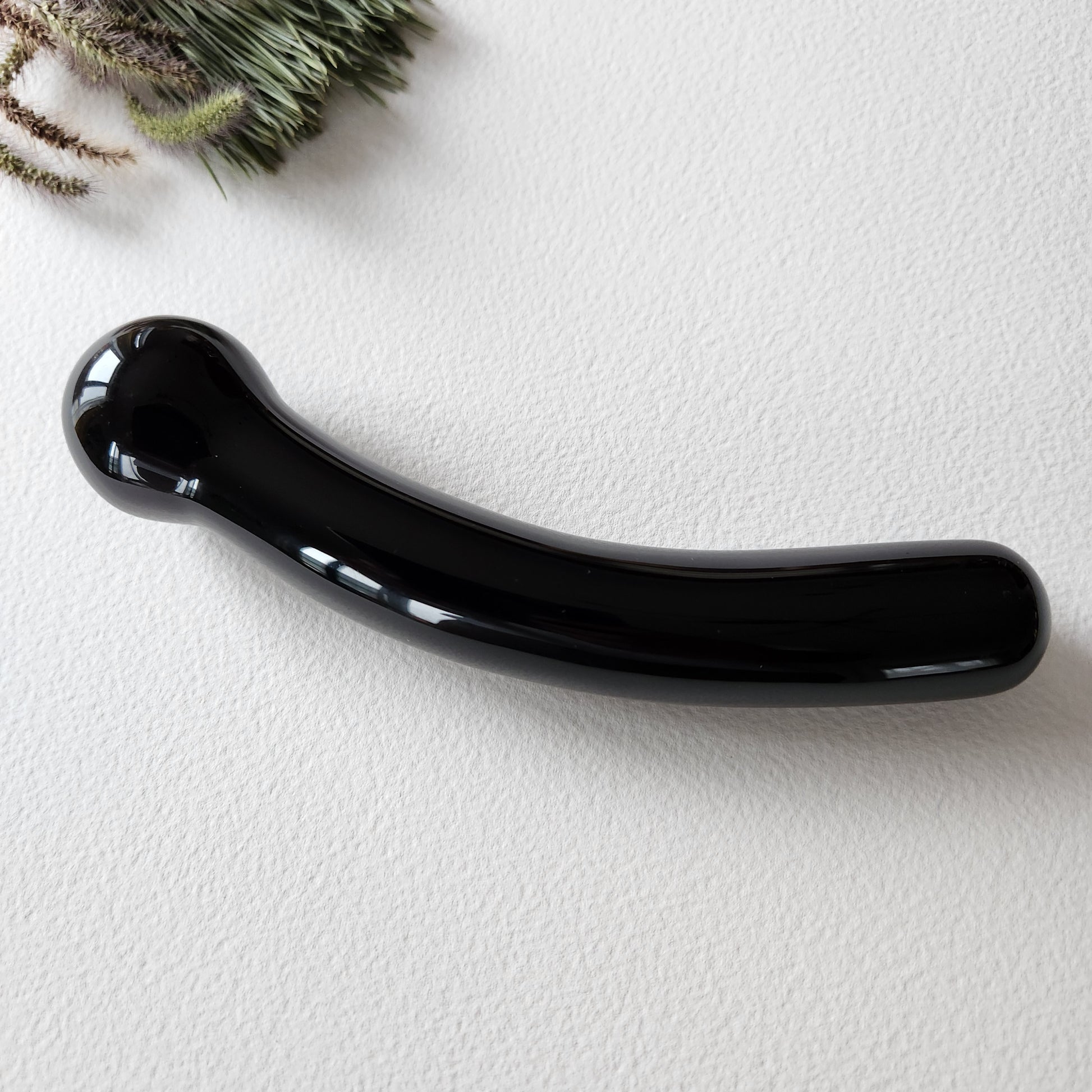 Close-up of a smooth, black curved obsidian crystal massage wand with round tip