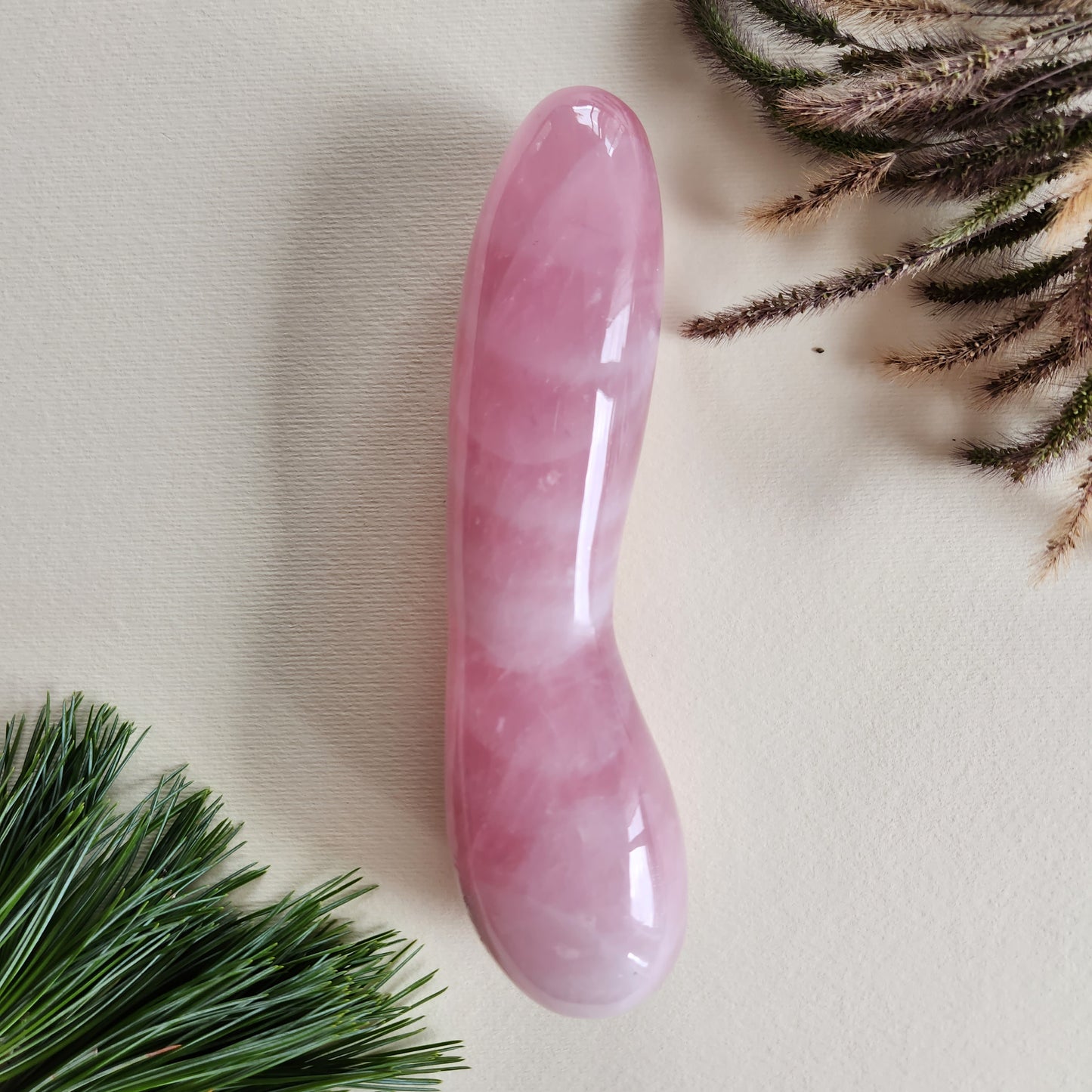 A long, smooth, pink Rose Quartz curved crystal massage wand, photographed on a neutral background.