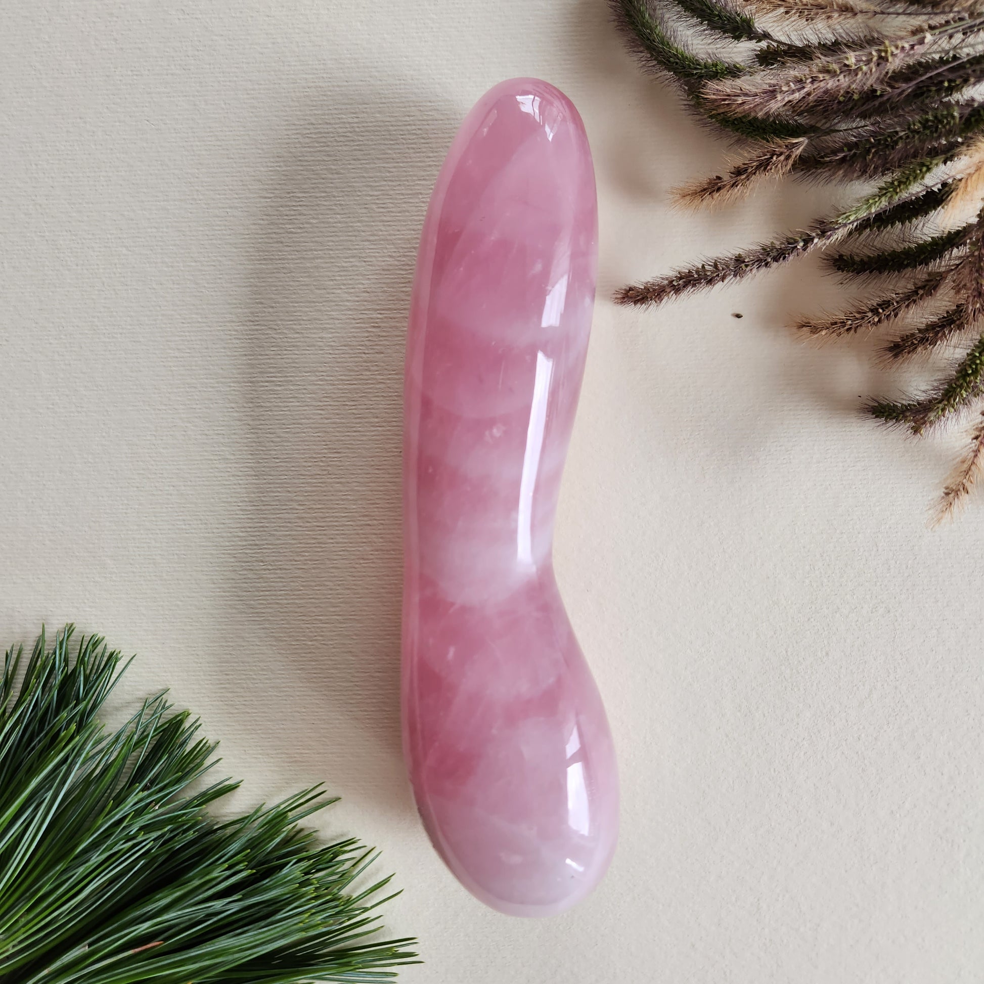 A long, smooth, pink Rose Quartz curved crystal massage wand, photographed on a neutral background.
