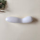 Large, polished white jade crystal wand with a unique contoured, spoon-like shape, lying on a light surface with pine needles and dried foliage.