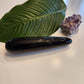 Thick, polished black obsidian crystal wand with a large diameter to reach the G-Spot, lying on a white surface next to a large green leaf and a rough amethyst geode.