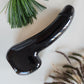 Polished black obsidian crystal wand in the shape of a phallus, perfect to reach the G-Spot, lying on a light surface with pine needles and dried grasses