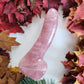 Polished rose quartz crystal wand in the shape of a phallus perfect for anal stimulation, surrounded by a border of colorful autumn leaves and pine needles on a white surface.